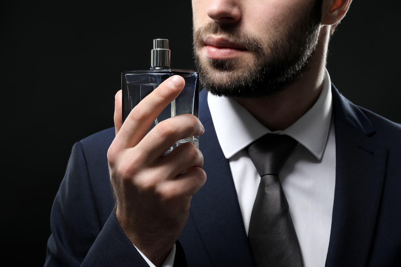 Man in Suit Holding Bottle of Perfume on Dark Background
